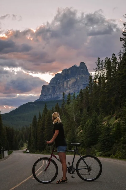 Kobieta na rowerze na drodze pod górami w zmierzchu