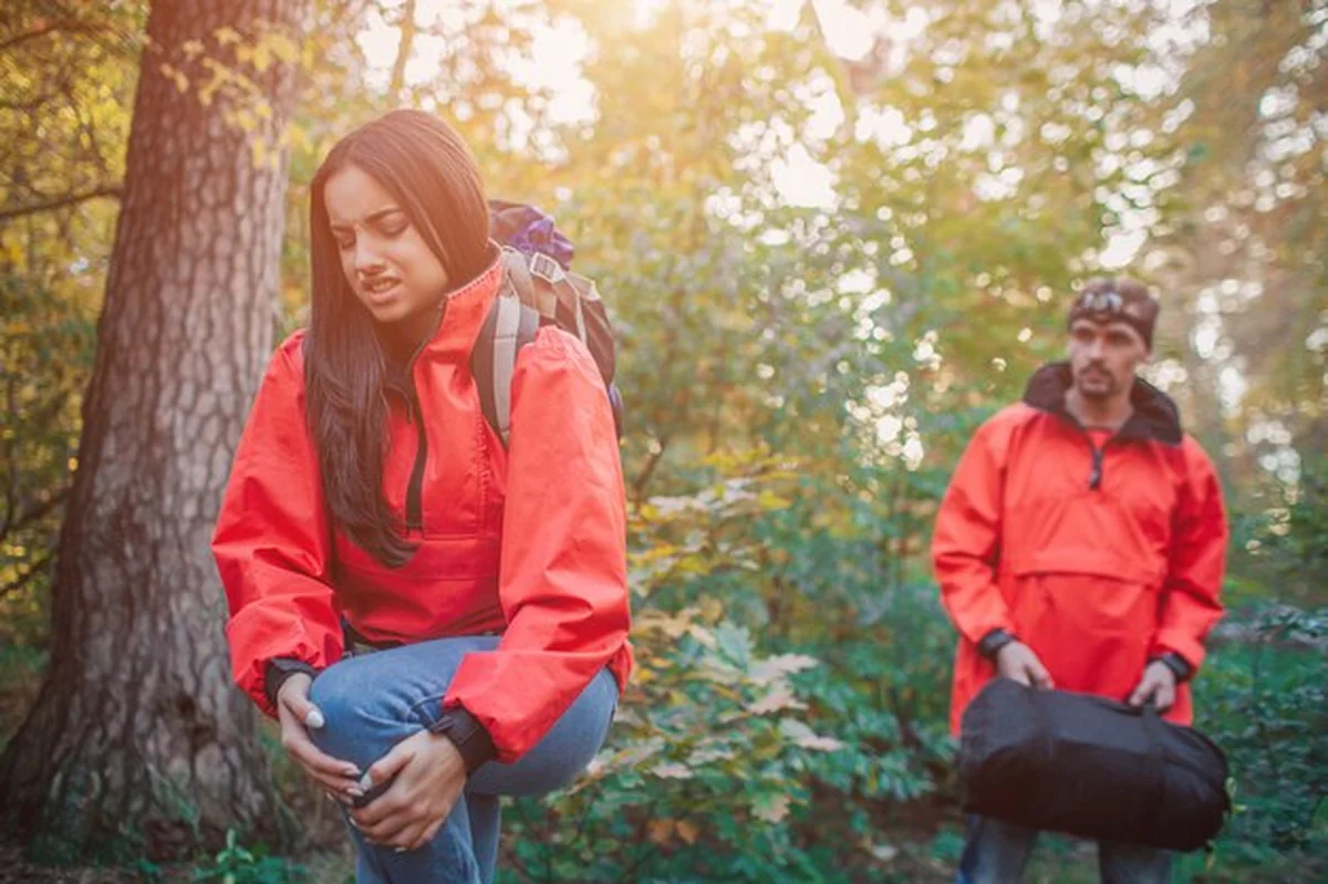 Młoda kobieta trzyma nogę z bólem, a facet z plecakiem patrzy na nią