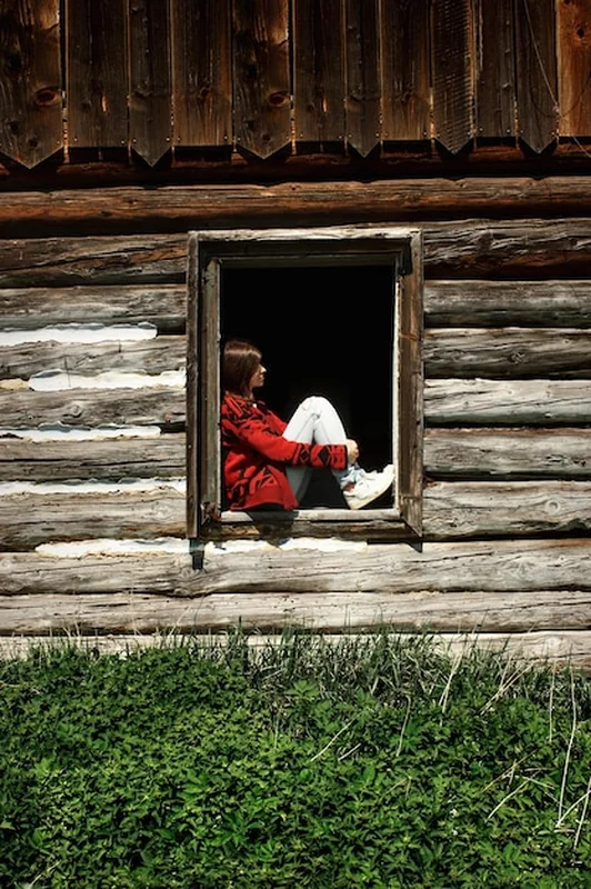 Kobieta siedząca na starym oknie w drewnianej chacie w górach