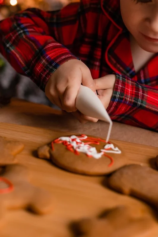 Chłopiec w czerwonej piżamie dekoruje ciasteczka w kuchni