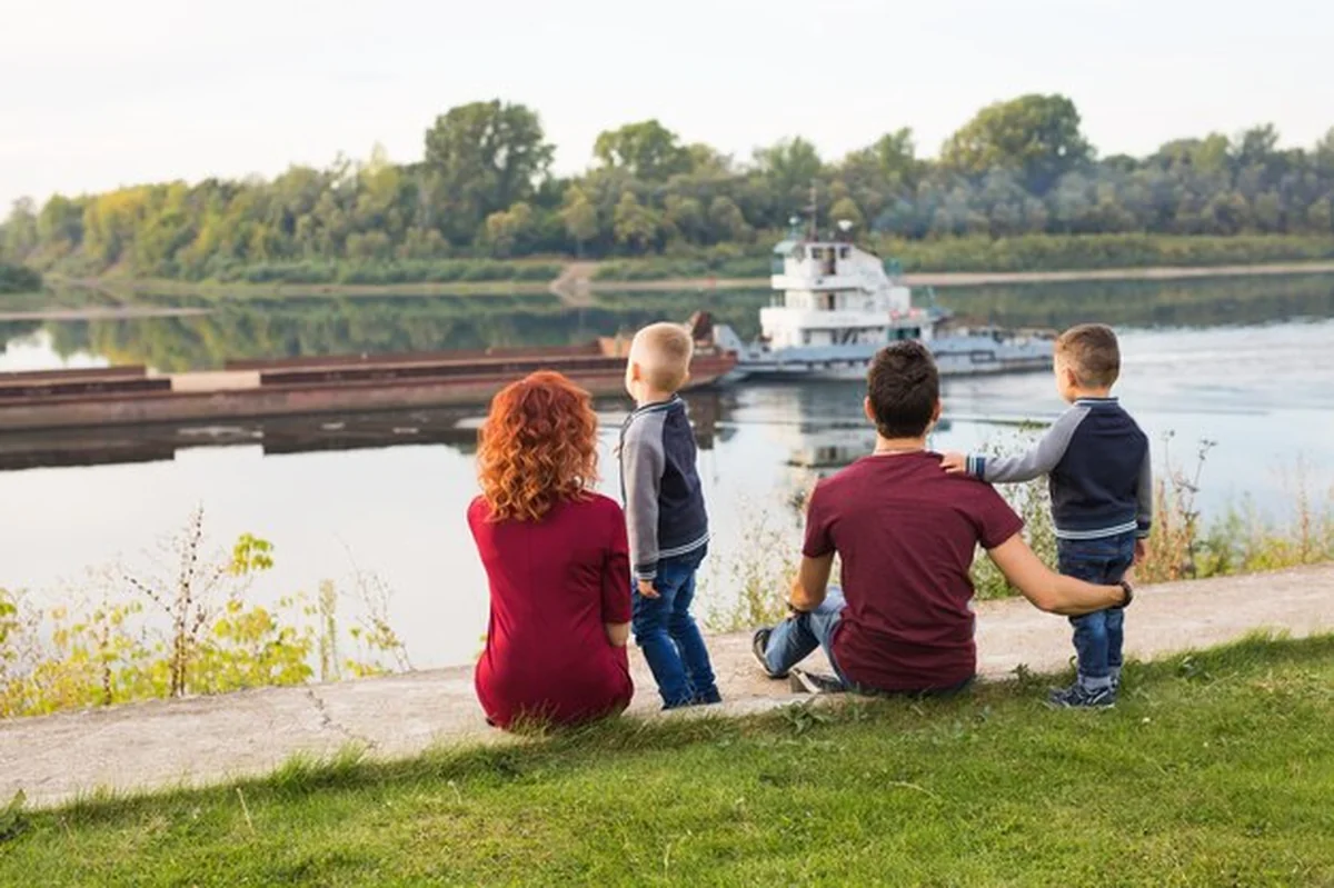 Rodzina siedzi na zieleni i patrzy na łódkę