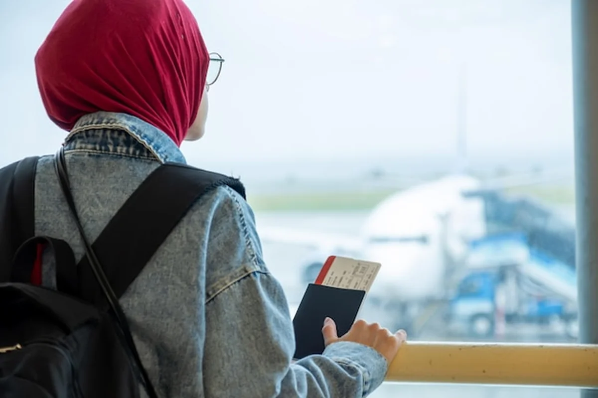 Arabka muzułmanka na lotnisku z paszportem i patrząca na samolot