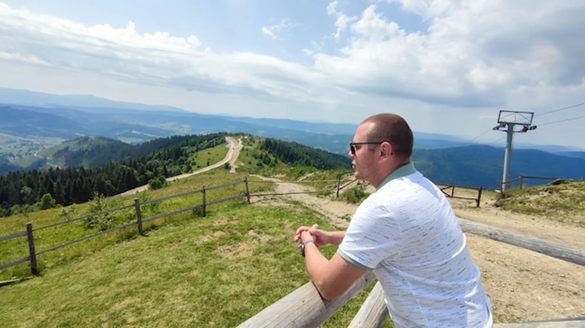 Turysta stoi na wzgórzu w trawie z widokiem na dolinę górską Karpat