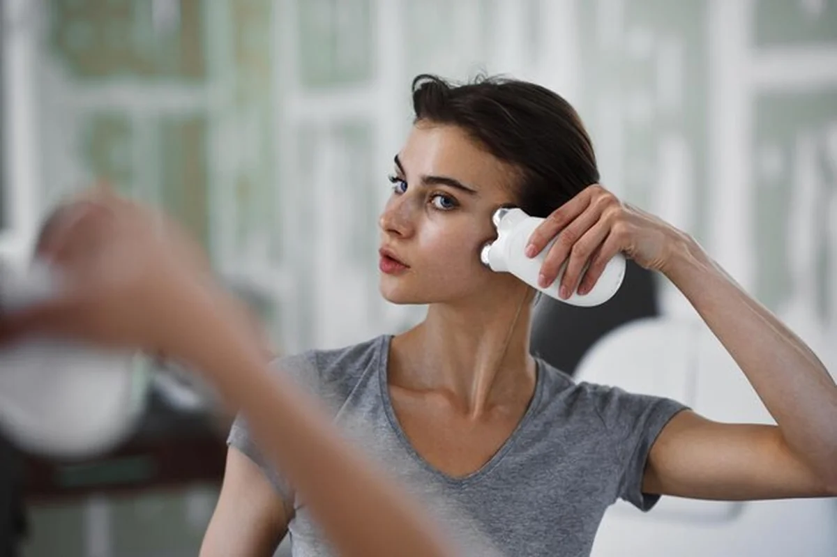 Kobieta masuje twarz za pomocą masażera z mikro prądem