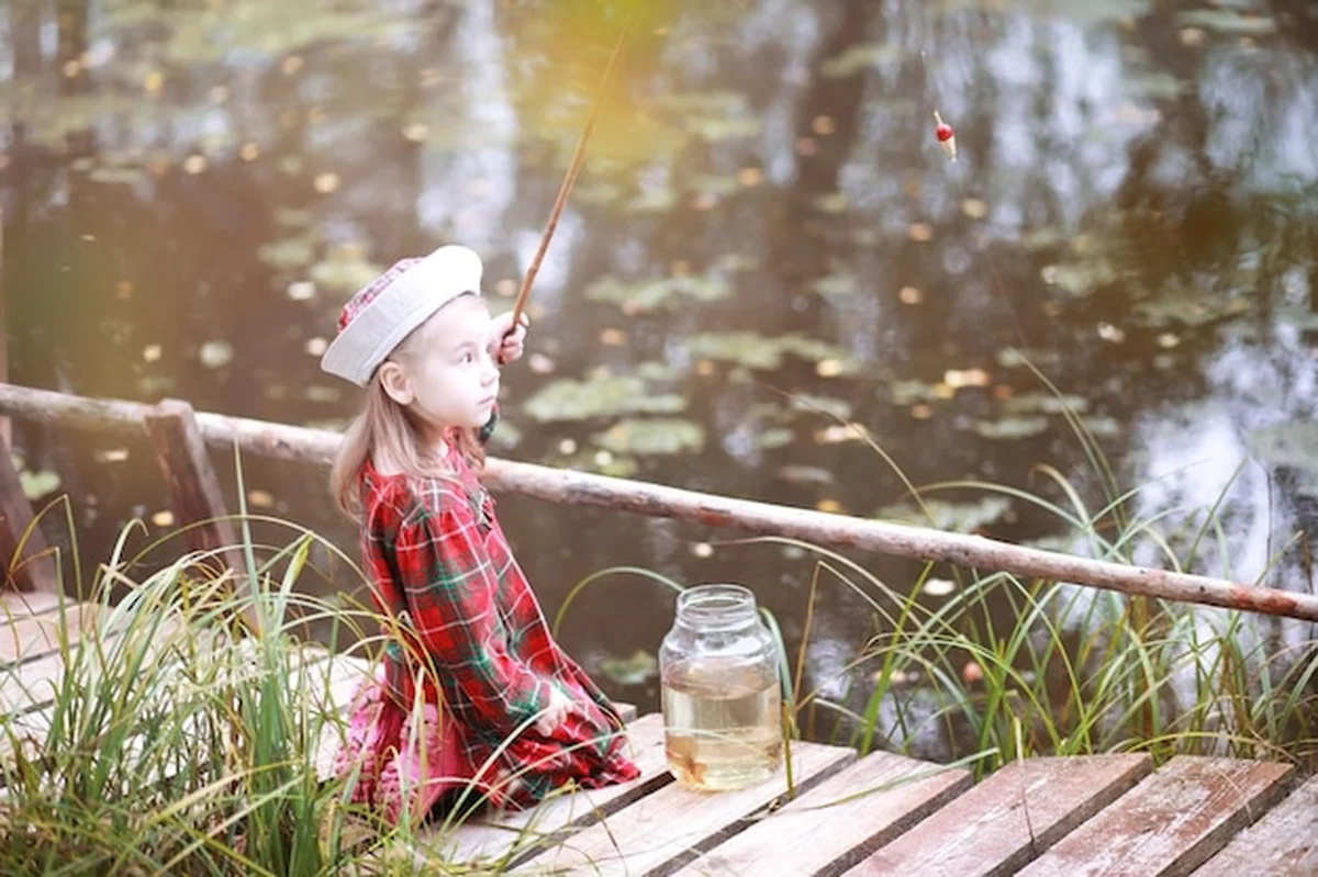 Dziecko łowi ryby nad stawem w jesienny poranek. Rybak z wędką na chodniku