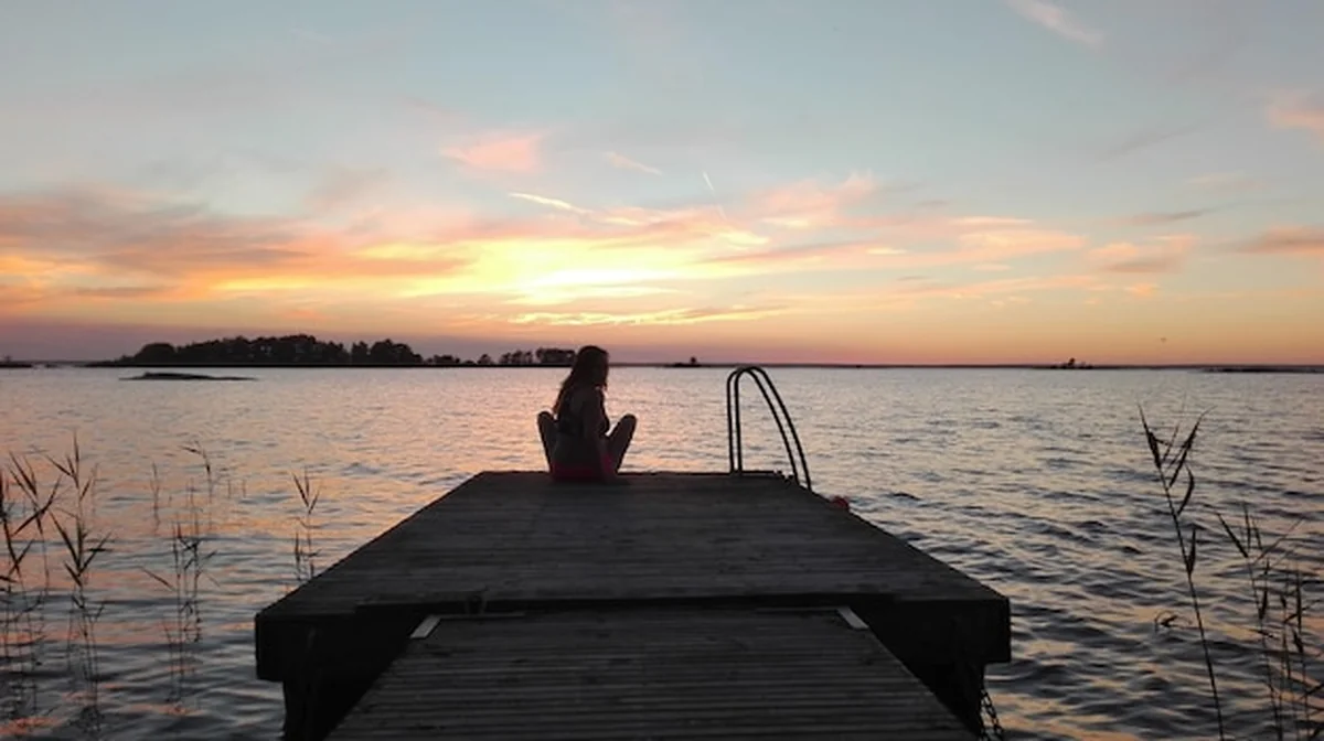 Kobieta siedząca na molo nad morzem podczas zachodu słońca