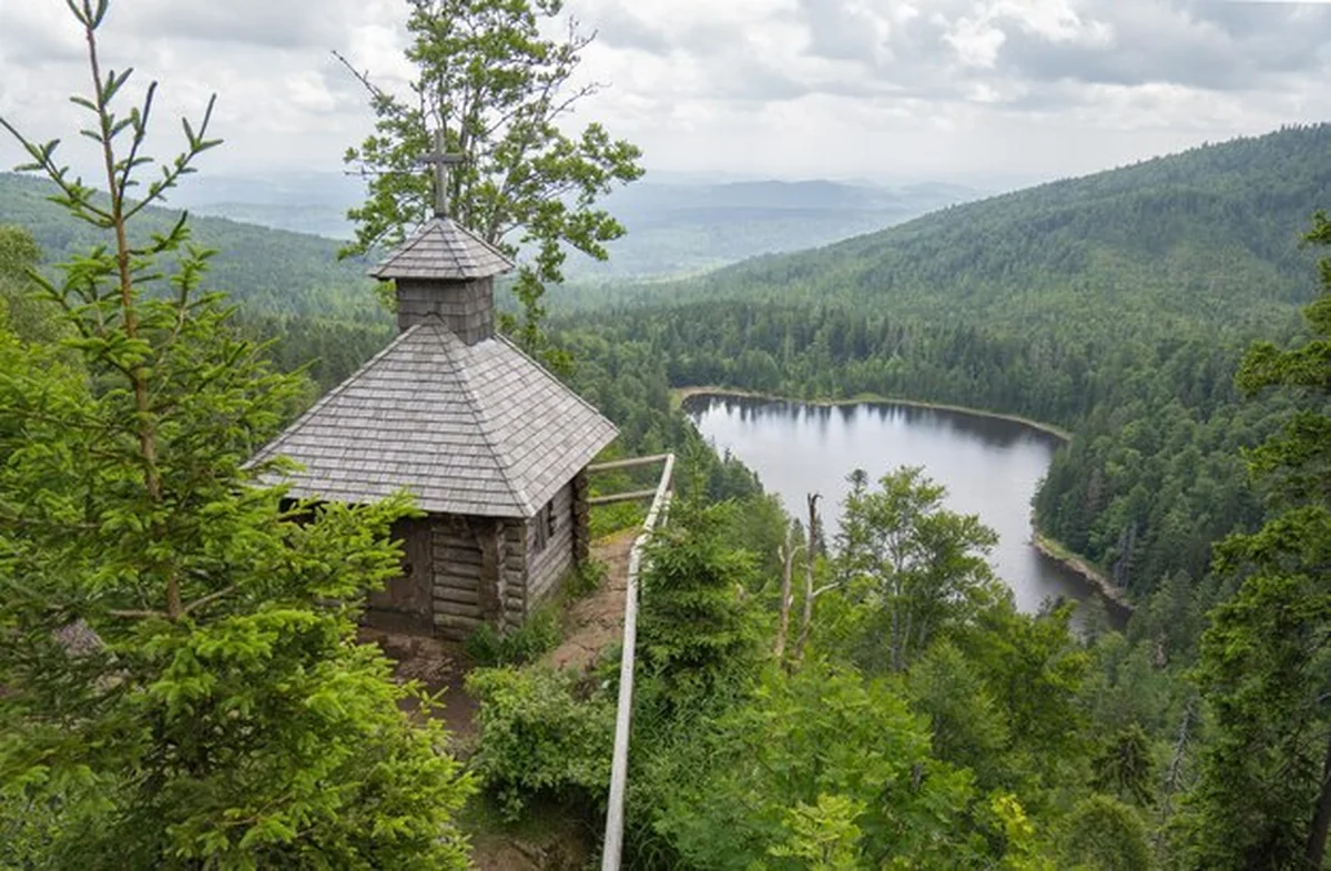 Drewniana kaplica w zielonym lesie z widokiem na jezioro
