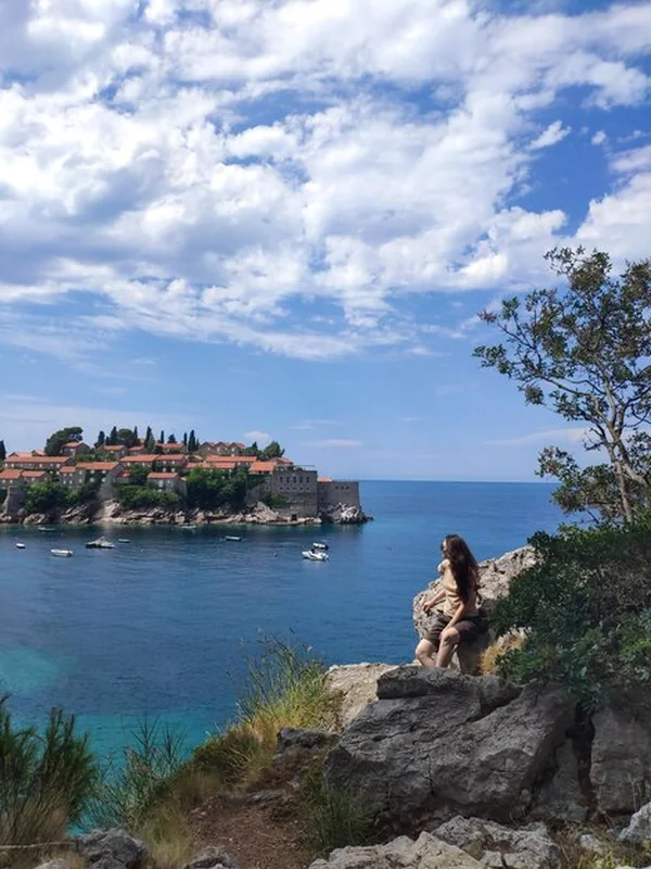 Kobieta siedzi na skale i patrzy na wyspę Sveti Stefan w Czarnogórze