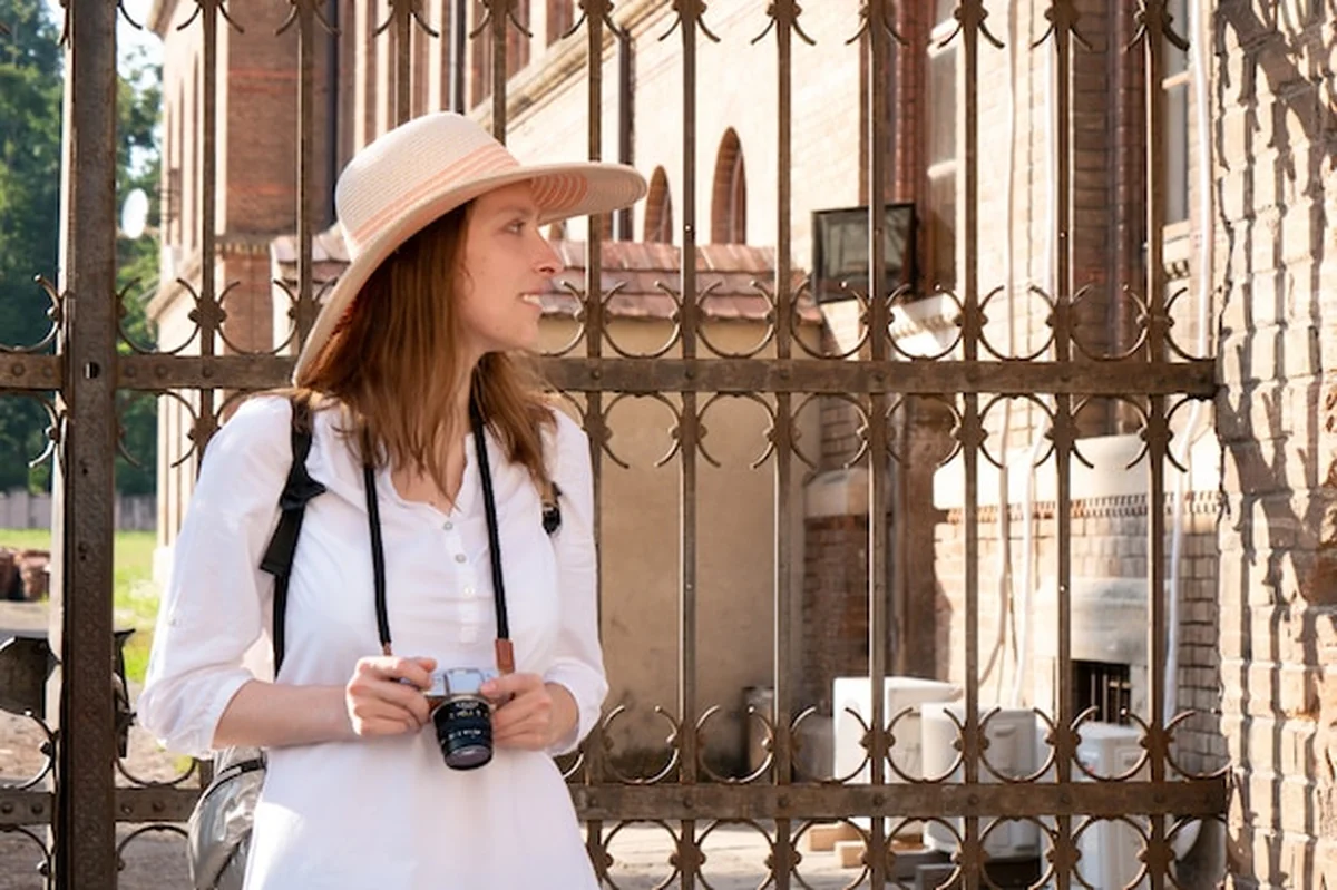 Kobieta w kapeluszu i białej bluzie z plecakiem podróżuje i robi zdjęcia