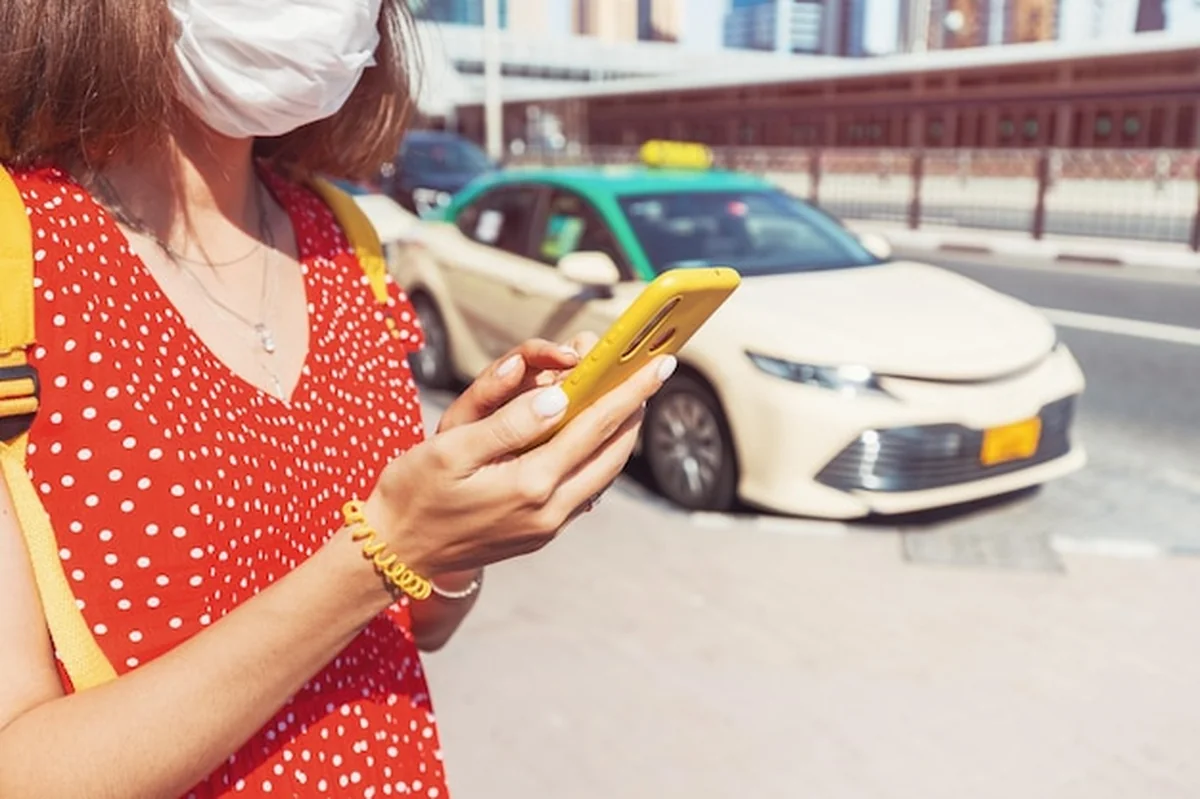 Turystka w medycznej masce wzywa taksówkę przez aplikację na smartfonie
